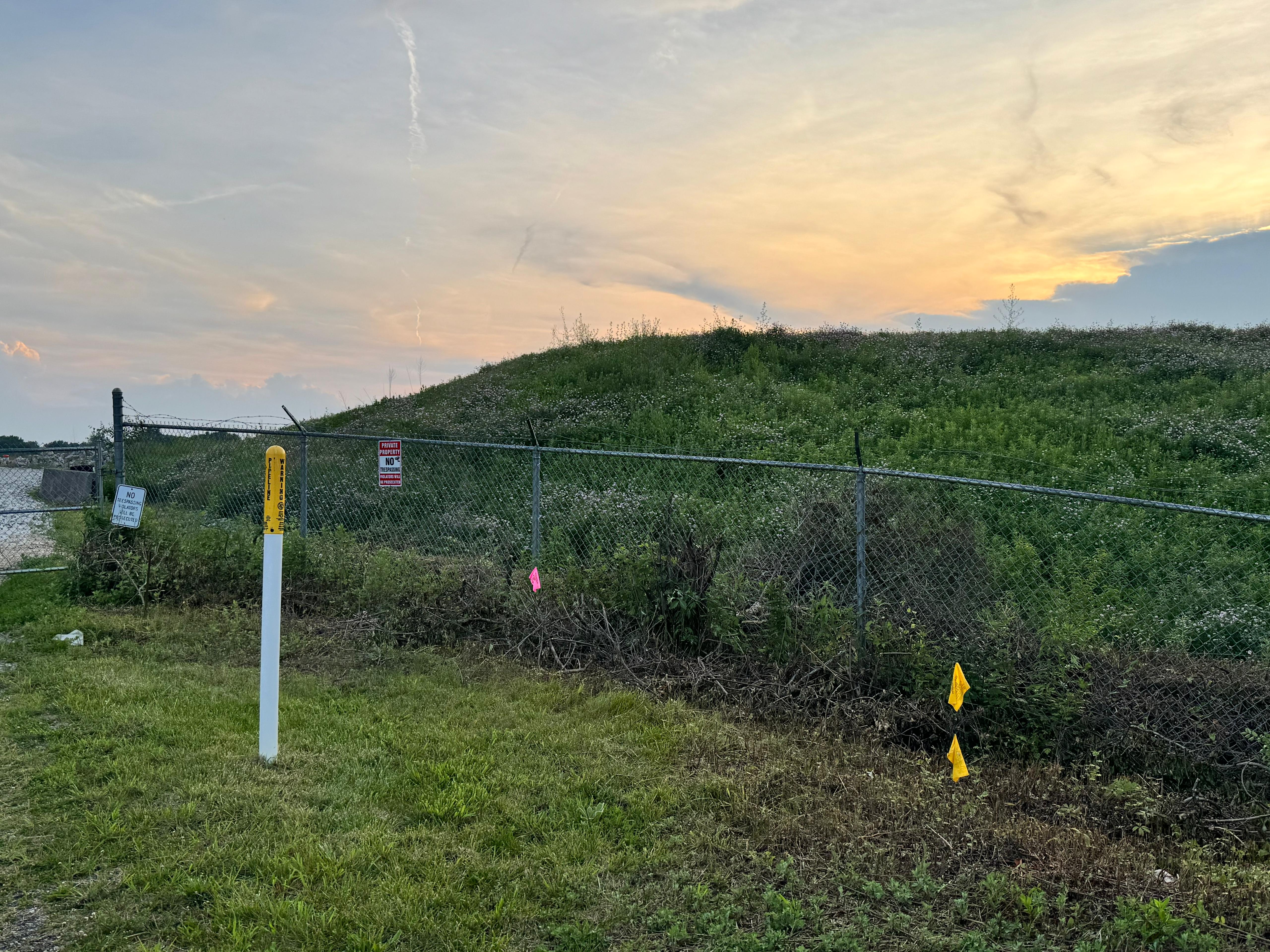 The fenced, capped mound at the Foote Mineral site at sunset, with pipeline and no-trespassing warning signs.